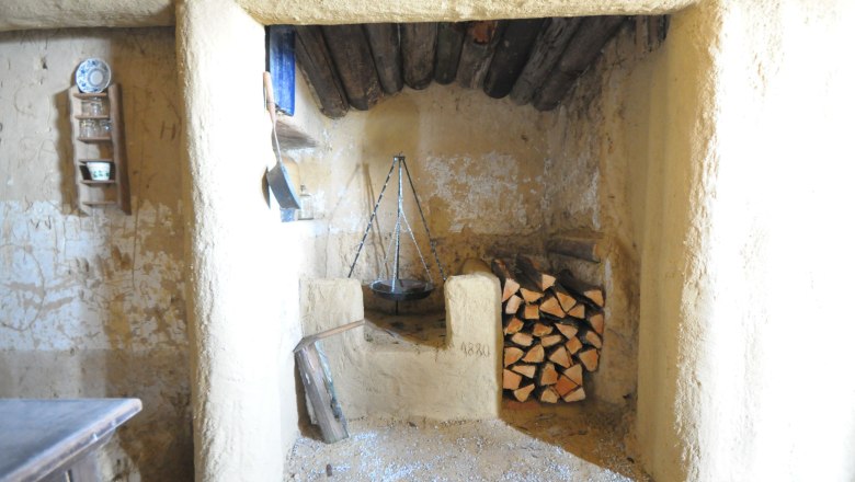 Innenansicht eines rustikalen Raumes mit Kamin und Holzstapel.