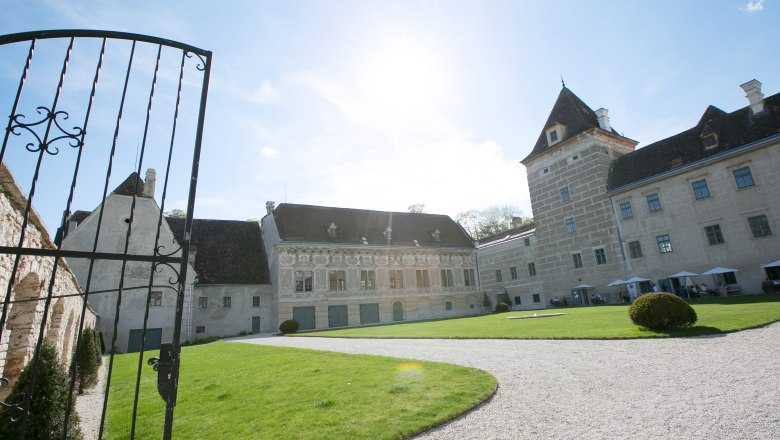 Eingang von Schloss Walpersdorf mit offenem Tor, Rasenfläche und historischem Gebäude im Hintergrund.