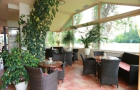 Ein heller Wintergarten mit Korbmöbeln und vielen Pflanzen.