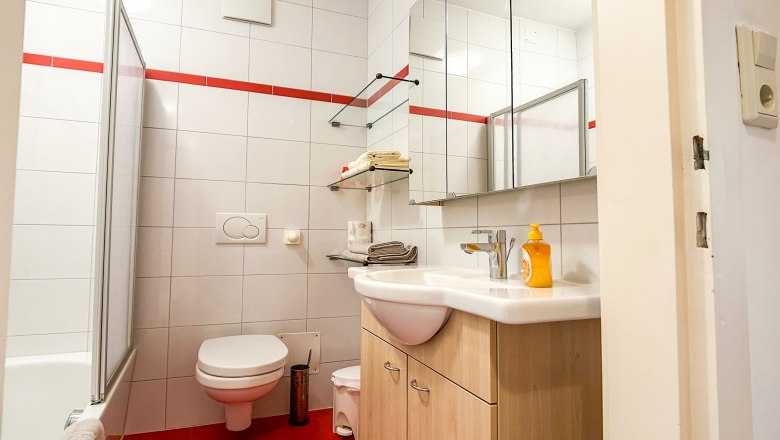 Modernes Badezimmer mit roten Fliesen, weißer Keramik und Spiegeln.