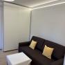 Modernes Wohnzimmer mit braunem Sofa, gelben Kissen und kleinem Tisch mit weißer Tischdecke.