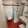 Badezimmer mit rotem Fliesenboden, weiß gefliesten Wänden, Dusche, Waschbecken und Toilette.