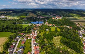Luftaufnahme einer ländlichen Region mit Feldern, einem See und einem Schloss auf einem Hügel.