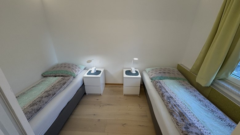 Schlafzimmer mit zwei Einzelbetten, Nachttisch und Lampen.