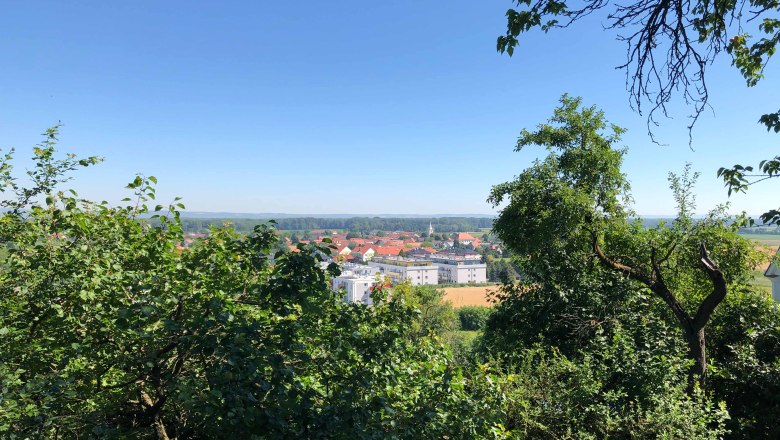 Blick auf eine Stadt mit roten D&auml;chern, umgeben von gr&uuml;nen B&auml;umen und blauem Himmel.