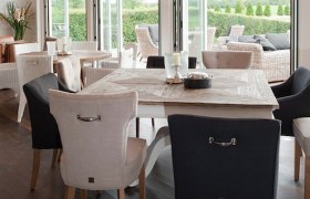 Innenraum mit Esstisch und Stühlen, Blick auf Terrasse mit Sitzmöbeln.