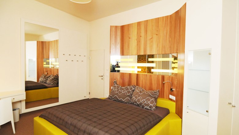 Modern eingerichtetes Schlafzimmer mit gelbem Bett und Holzverkleidung an der Wand.
