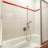 Badezimmer mit Badewanne, Duschkopf und roten Fliesen.
