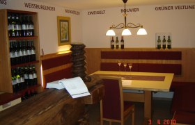Innenansicht eines Weinguts mit Tisch, Stühlen und Weinregalen.