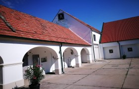 Wei&szlig;es Geb&auml;ude mit roten Ziegeld&auml;chern und Arkaden, blauer Himmel.