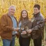Drei Personen stoßen mit Weingläsern in einem herbstlichen Weinberg an.