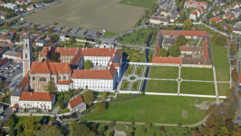 Luftaufnahme eines großen Gebäudekomplexes mit roten Dächern und Gartenanlagen.