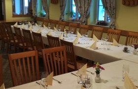 Ein festlich gedeckter Saal mit langen Tischen, St&uuml;hlen und dekorativen Vorh&auml;ngen.