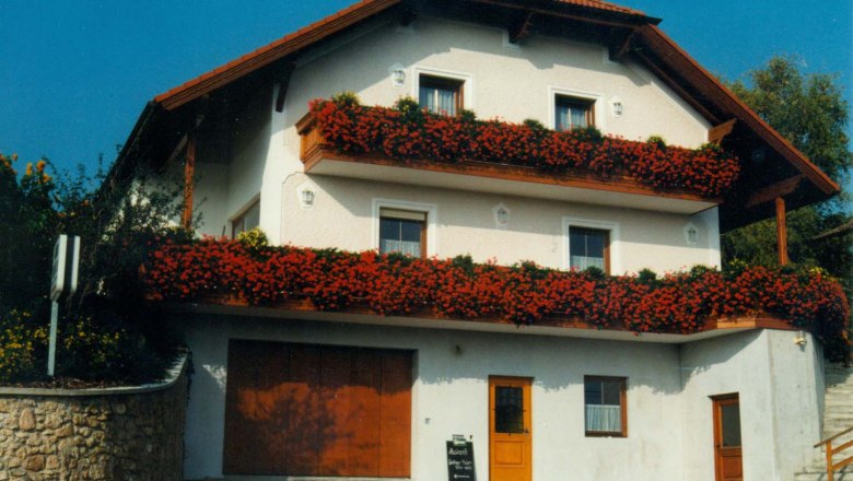Ein zweistöckiges Gästehaus mit roten Blumen auf den Balkonen.