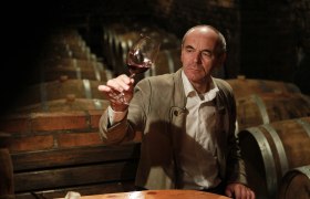 Ein Mann im Weinkeller hält ein Glas Rotwein hoch.