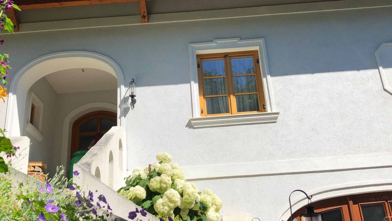 Haus mit wei&szlig;en W&auml;nden, Holzdach und Blumen im Vordergrund.