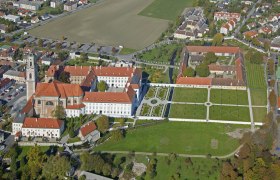 Luftaufnahme eines großen Gebäudekomplexes mit roten Dächern und Gartenanlagen.