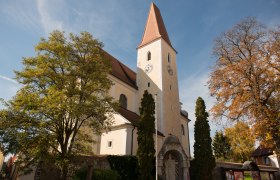 Kirche mit Turm und Uhr, umgeben von B&auml;umen im Herbst.