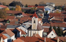 Luftaufnahme der Pfarrkirche Getzersdorf mit umliegenden Häusern und Feldern im Herbst.