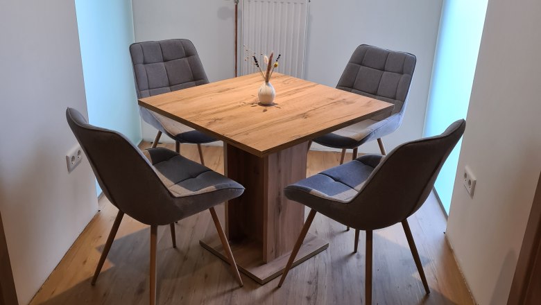 Ein moderner Esstisch mit vier grauen Stühlen in einem hellen Raum.