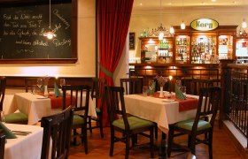 Gemütliches Restaurant mit Holzmöbeln, gedeckten Tischen und einer Bar im Hintergrund.