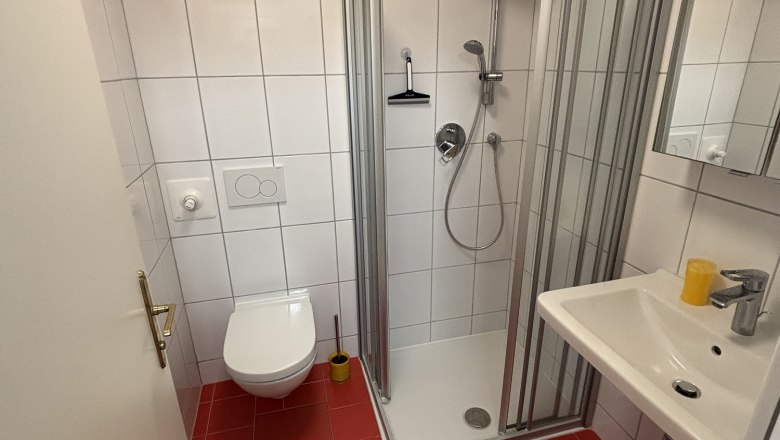 Badezimmer mit rotem Fliesenboden, weiß gefliesten Wänden, Dusche, Waschbecken und Toilette.