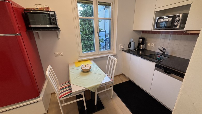 Kleine Küche mit rotem Kühlschrank, Tisch, Stühlen und Fenster.