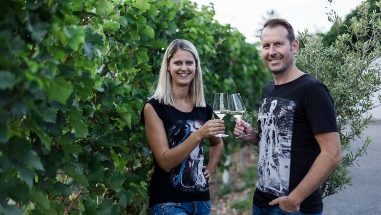 Zwei Personen sto&szlig;en mit Weingl&auml;sern in einem Weinberg an.