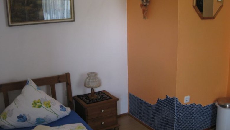 Ein kleines Zimmer mit einem Einzelbett, Nachttisch, Lampe und orangefarbener Wand mit Mosaikfliesen.