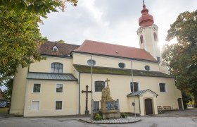 Pfarrkirche Heiligeneich mit Statue und Kreuz im Vordergrund.