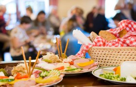Ein Tisch mit traditionellen österreichischen Speisen, darunter Aufschnitt, Käse und Brot in einem Korb mit rot-weiß kariertem Tuch.
